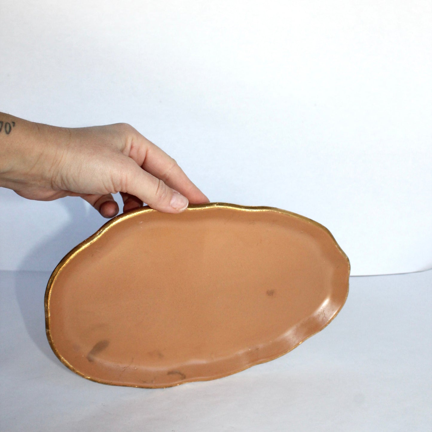 Hand holding a terracotta-colored concrete plate on a white background