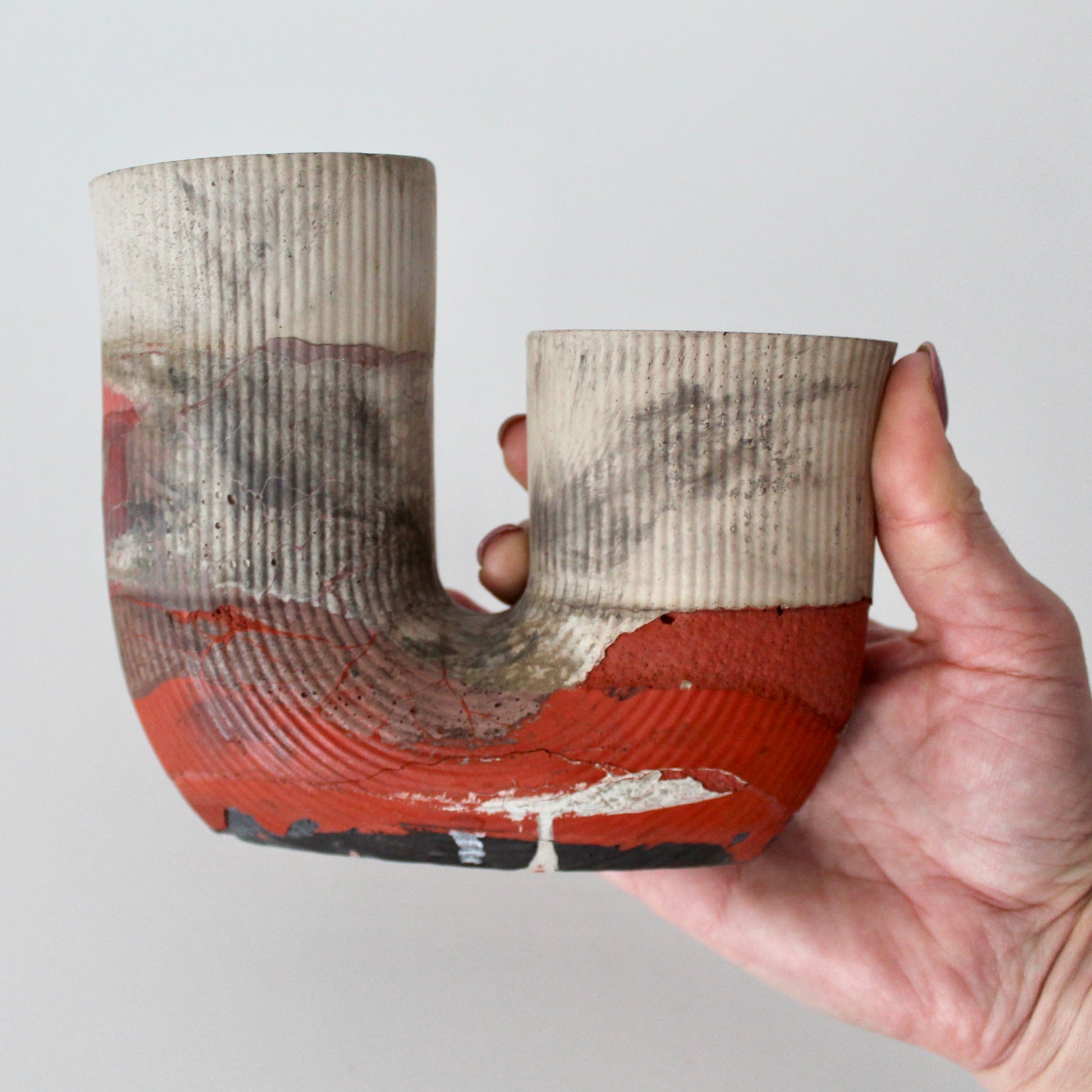 Hand holding a unique cement vase with a U-shaped design against a plain background