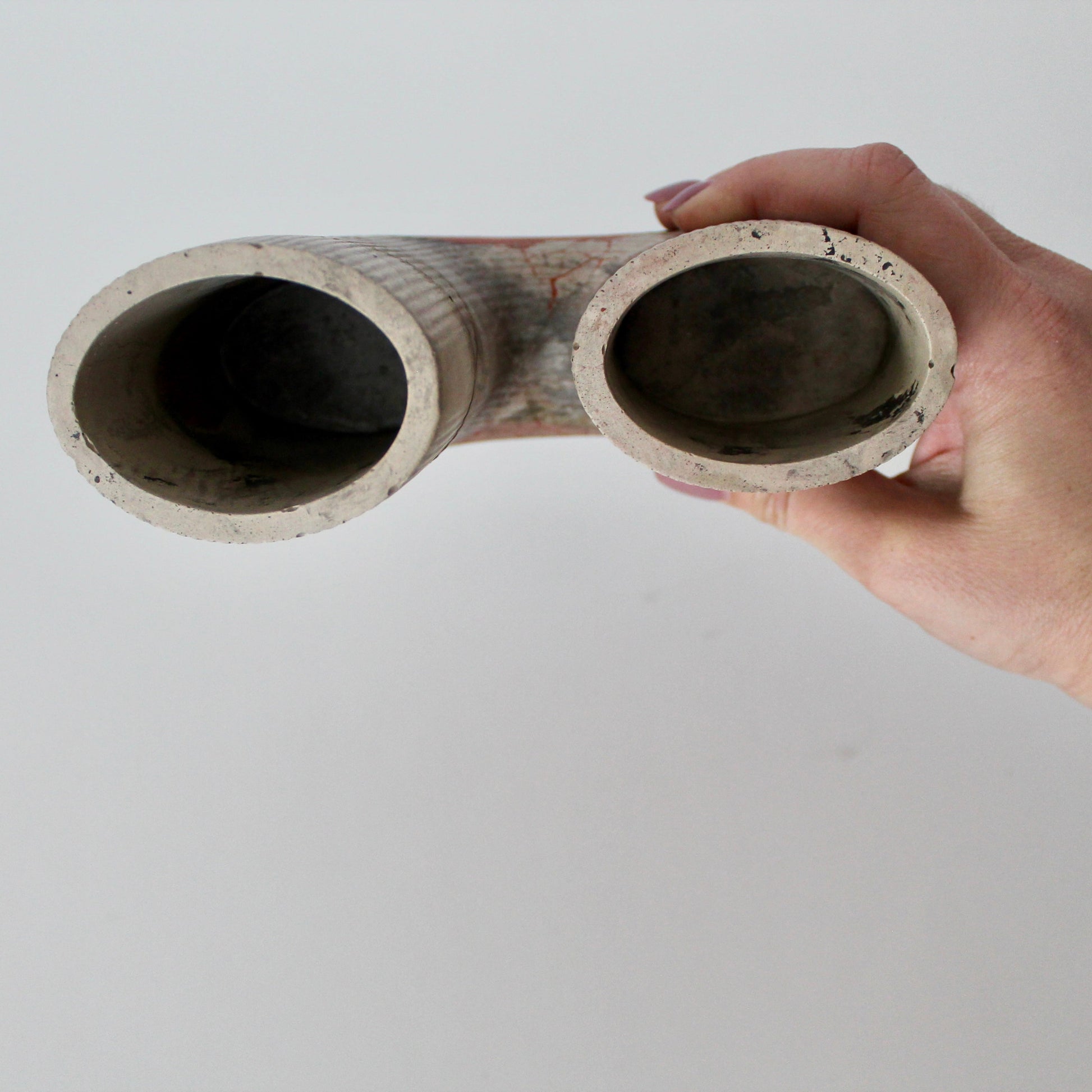 Hand holding a concrete vase with two openings against a plain background