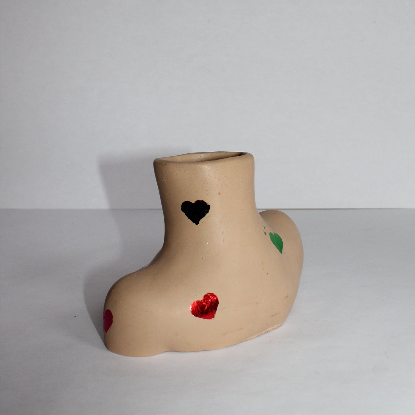 concrete woman shaped vase with decorative colored hearts on a plain background
