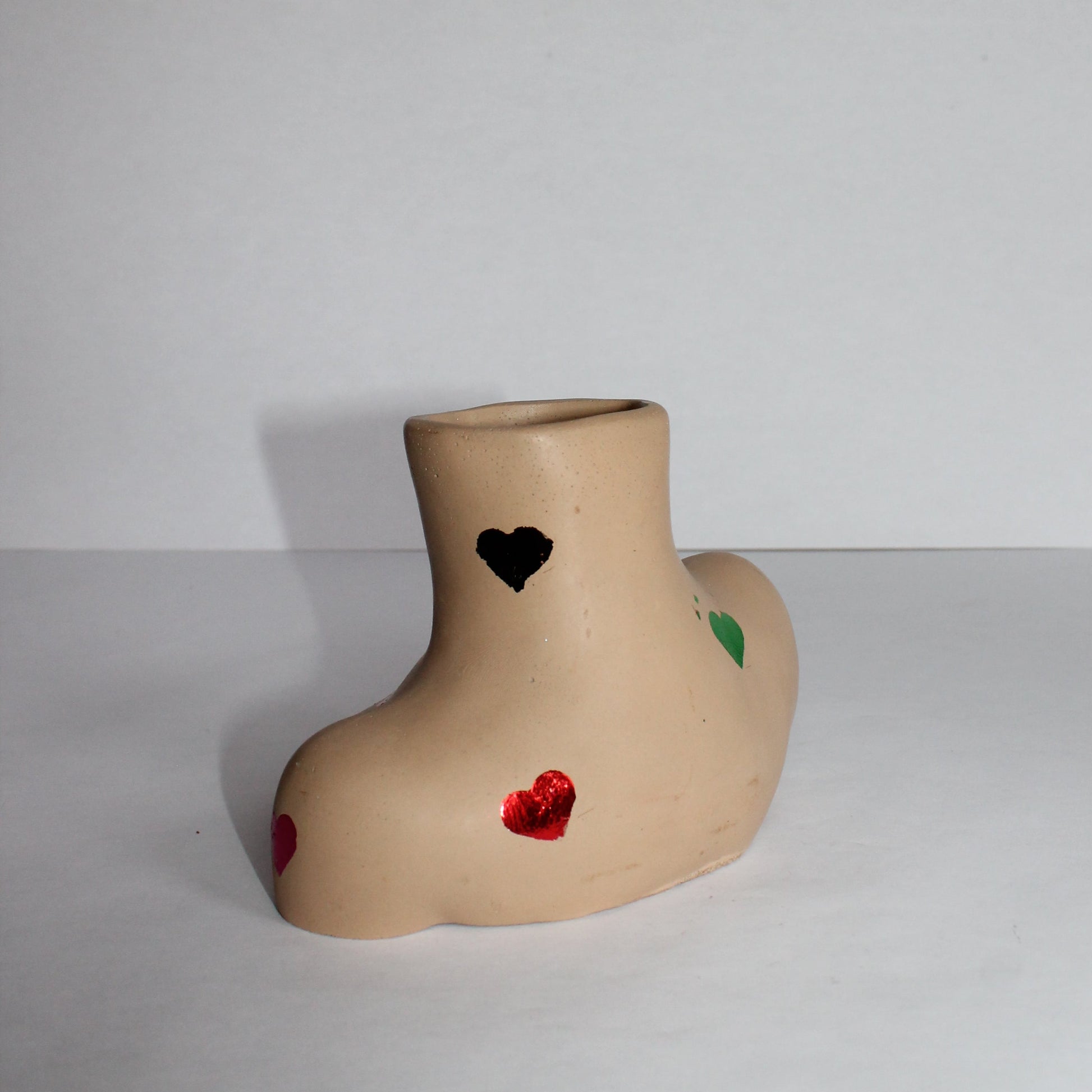 concrete woman shaped vase with decorative colored hearts on a plain background